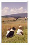 1960s Back Of Two Boys With Black And White Dog Sitting Hillside Field Looking Down To Farm by Anonymous