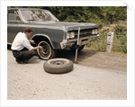 1960s Man Changing Flat Tire On Car At Side Of Rural Road Car Jack Tools Tire Iron by Anonymous