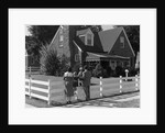 1950s Family Standing By White Fence Looking At Brick House by Anonymous