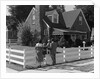 1950s Family Standing By White Fence Looking At Brick House by Anonymous