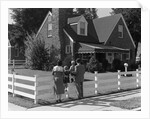 1950s Family Standing By White Fence Looking At Brick House by Anonymous