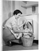 1950s Woman Kneeling Removing Clothes Laundry From Automatic Dryer by Anonymous