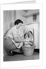 1950s Woman Kneeling Removing Clothes Laundry From Automatic Dryer by Anonymous