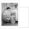 1950s Woman Kneeling Removing Clothes Laundry From Automatic Dryer by Anonymous