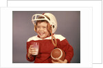 1950s 1960s Boy Drinking Milk Wearing Football Helmet Red Jersey Holding Ball by Anonymous