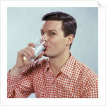 1960s Man Drinking Glass Water Wearing Red Checkered Shirt by Anonymous