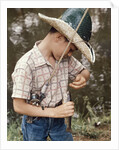 Boy Wearing Straw Hat Removing Hook From Mouth Of Fish Outdoor by Anonymous
