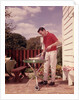 1960s Man Wearing Red Shirt Cooking Steak Outdoor On Backyard Grill by Anonymous