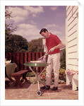 1960s Man Wearing Red Shirt Cooking Steak Outdoor On Backyard Grill by Anonymous