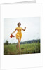 1970s Young Woman Wearing Colorful Print Dress Running In Field Carrying Red Straw Hat by Anonymous