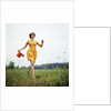 1970s Young Woman Wearing Colorful Print Dress Running In Field Carrying Red Straw Hat by Anonymous