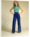 1970s Young Woman With Long Curly Hair Standing Hands On Hips In Bell Bottom Denim Blue Jeans by Anonymous