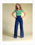 1970s Young Woman With Long Curly Hair Standing Hands On Hips In Bell Bottom Denim Blue Jeans by Anonymous