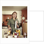 1960s Young Housewife While Checking Grocery Shopping Receipt In Kitchen by Anonymous