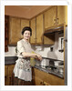1960s Woman Housewife Wearing An Apron Stirring Cooking Pot At Kitchen Stove by Anonymous