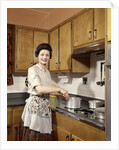 1960s Woman Housewife Wearing An Apron Stirring Cooking Pot At Kitchen Stove by Anonymous