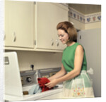1970s Woman Housewife Homemaker Wearing Apron Loading Laundry Into Washing Machine by Anonymous