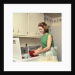 1970s Woman Housewife Homemaker Wearing Apron Loading Laundry Into Washing Machine by Anonymous