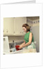 1970s Woman Housewife Homemaker Wearing Apron Loading Laundry Into Washing Machine by Anonymous