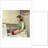1970s Woman Housewife Homemaker Wearing Apron Loading Laundry Into Washing Machine by Anonymous