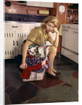 1960s Weary Dejected Woman Housewife Homemaker Sitting On Full Laundry Basket In Kitchen by Anonymous