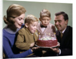 1960s Mother And Father Holding Birthday Cake And Sons Blowing Out Candles by Anonymous