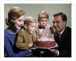 1960s Mother And Father Holding Birthday Cake And Sons Blowing Out Candles by Anonymous