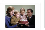 1960s Mother And Father Holding Birthday Cake And Sons Blowing Out Candles by Anonymous