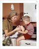1970s Mother Giving First-Aid Putting Band-Aid On Knee Of Son In Kitchen by Anonymous