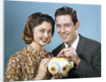 1950s 1960s Young Couple Man And Woman Put Quarter In Savings Piggy Bank by Anonymous