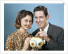 1950s 1960s Young Couple Man And Woman Put Quarter In Savings Piggy Bank by Anonymous