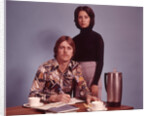 1970s Husband Wearing Loud Print Shirt Writing Family Budget and Wife Standing Behind Coffee Pot by Anonymous
