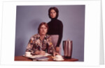 1970s Husband Wearing Loud Print Shirt Writing Family Budget and Wife Standing Behind Coffee Pot by Anonymous