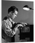 1940s Young Man Office File Clerk Putting Records Into Filing Cabinet Drawer by Anonymous