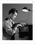 1940s Young Man Office File Clerk Putting Records Into Filing Cabinet Drawer by Anonymous