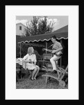 1960s Boy Playing Guitar, Woman Holding Soft Drink Bottle Outside In Backyard by Anonymous
