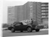 1960s Man In Suit and Hat Standing Beside Oldsmobile Toranado In Front Of Large Apartment Building by Anonymous