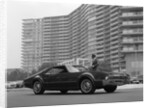 1960s Man In Suit and Hat Standing Beside Oldsmobile Toranado In Front Of Large Apartment Building by Anonymous