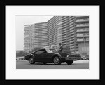 1960s Man In Suit and Hat Standing Beside Oldsmobile Toranado In Front Of Large Apartment Building by Anonymous