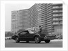 1960s Man In Suit and Hat Standing Beside Oldsmobile Toranado In Front Of Large Apartment Building by Anonymous
