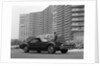 1960s Man In Suit and Hat Standing Beside Oldsmobile Toranado In Front Of Large Apartment Building by Anonymous