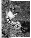 1920s Young Woman In Striped Skirt Sitting On Stream Bank In Woods Braiding Garland Of Wild Flowers by Anonymous