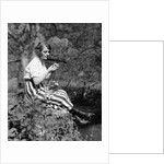 1920s Young Woman In Striped Skirt Sitting On Stream Bank In Woods Braiding Garland Of Wild Flowers by Anonymous