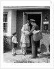 1950s Suburban Mom At Home Front Door With Son Watching Receiving Package From Mailman by Anonymous