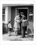 1950s Suburban Mom At Home Front Door With Son Watching Receiving Package From Mailman by Anonymous