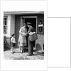 1950s Suburban Mom At Home Front Door With Son Watching Receiving Package From Mailman by Anonymous
