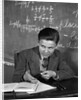 1920s 1930s Boy At Desk In Classroom In Front Of Blackboard Shooting Paper Wad With Rubber Band by Anonymous