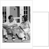 1930s Couple Man Woman In Tennis Whites Holding Racquets Sitting Talking On Steps In Front Of House Outdoor by Anonymous