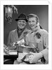 1950s Husband And Wife Carrying Armload Of Christmas Packages Standing In Snow Under Porch Light by Anonymous