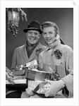 1950s Husband And Wife Carrying Armload Of Christmas Packages Standing In Snow Under Porch Light by Anonymous